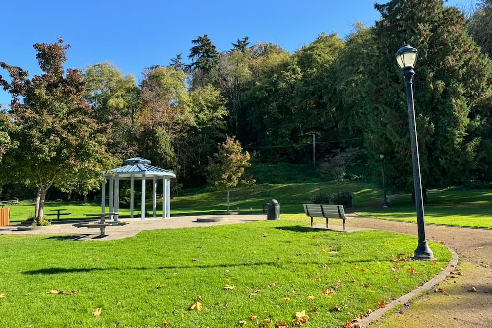 Grassy area next to the municipal parking lot with a shelter and picnic tables.