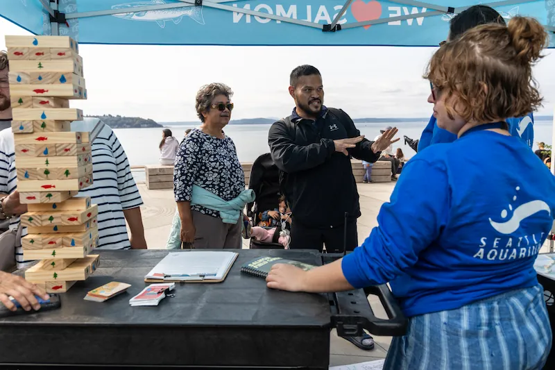 Two adults talk with Seattle Aquarium staff at a programming table on the rooftop of the Ocean Pavilion building.